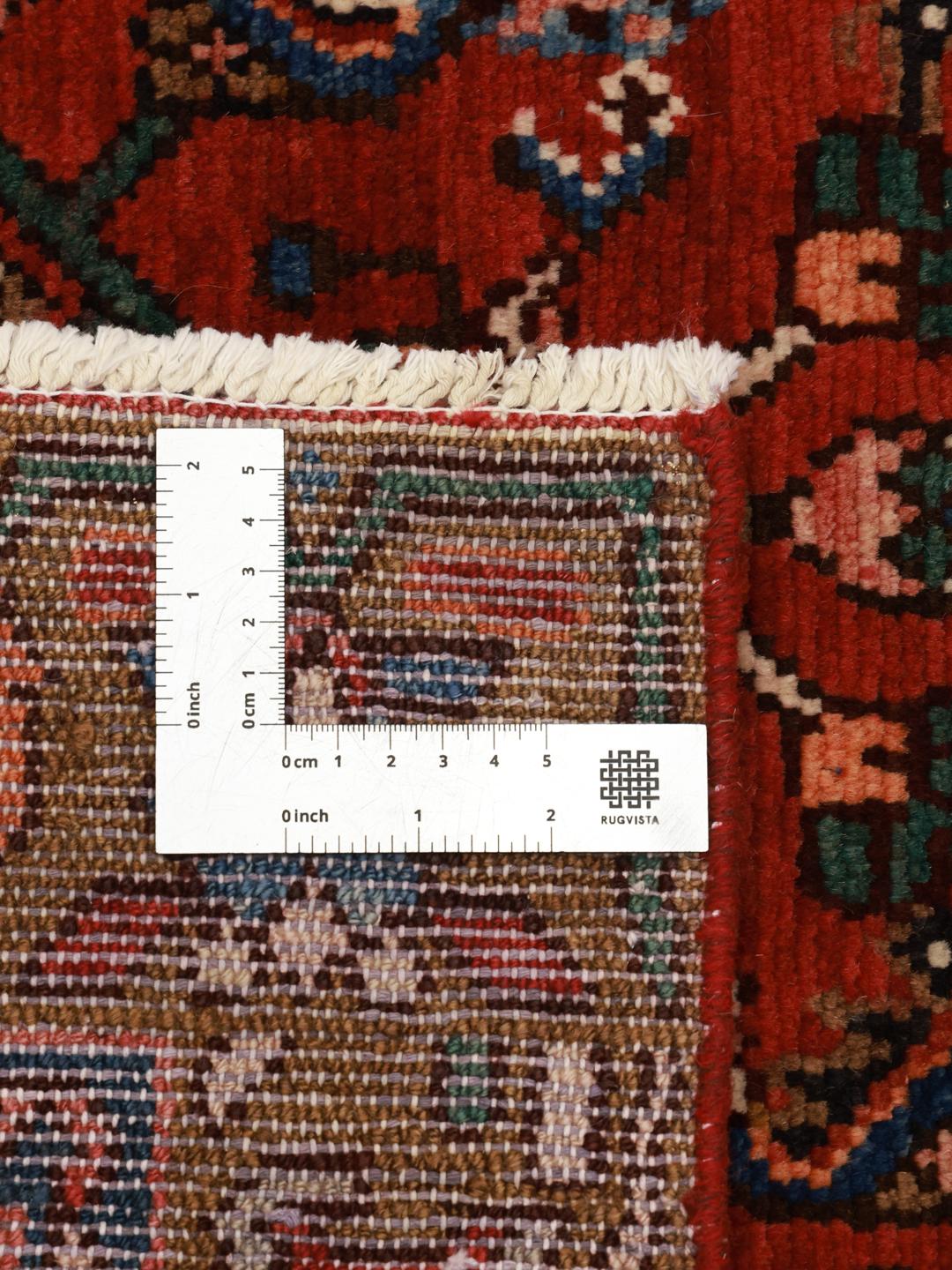 Et håndknyttet Hosseinabad-tæppe fra Mellemøsten med et rødt felt og traditionelle motiver.