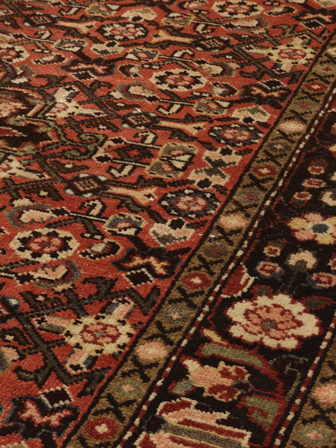 A hand-knotted Hosseinabad rug from the Middle East featuring a red and dark-toned floral design