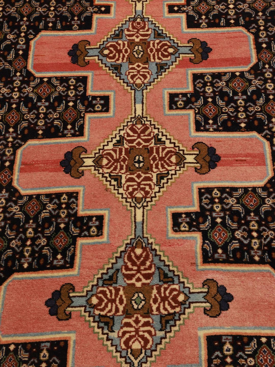 A hand-knotted Senneh runner with a multicolored diamond pattern on a dark field.