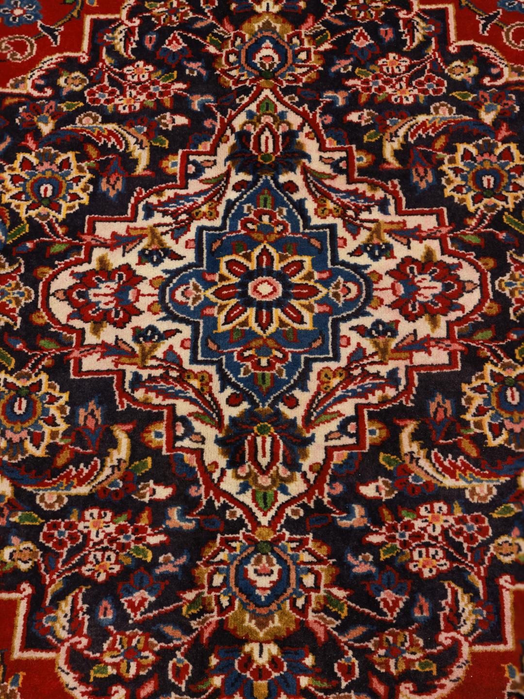 A large, hand-knotted Keshan rug from the Middle East with a red field and ornate floral patterns.