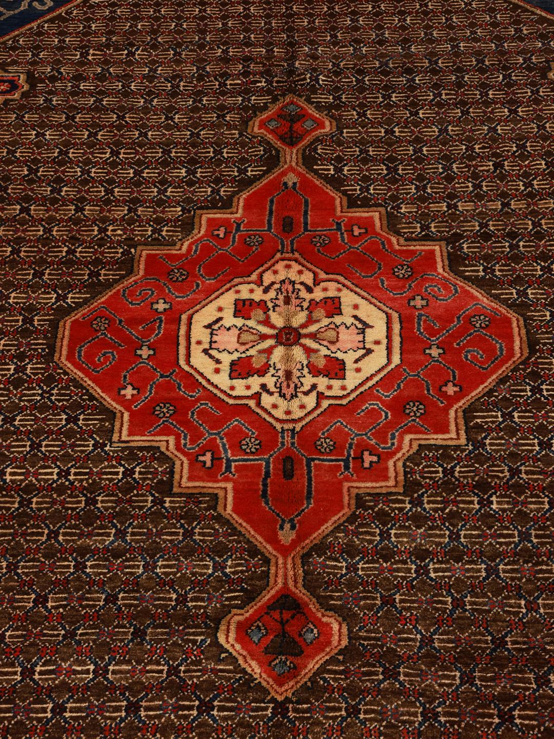Een handgeknoopt Koliai tapijt met ingewikkelde geometrische motieven in diepblauw, rood en bruin.