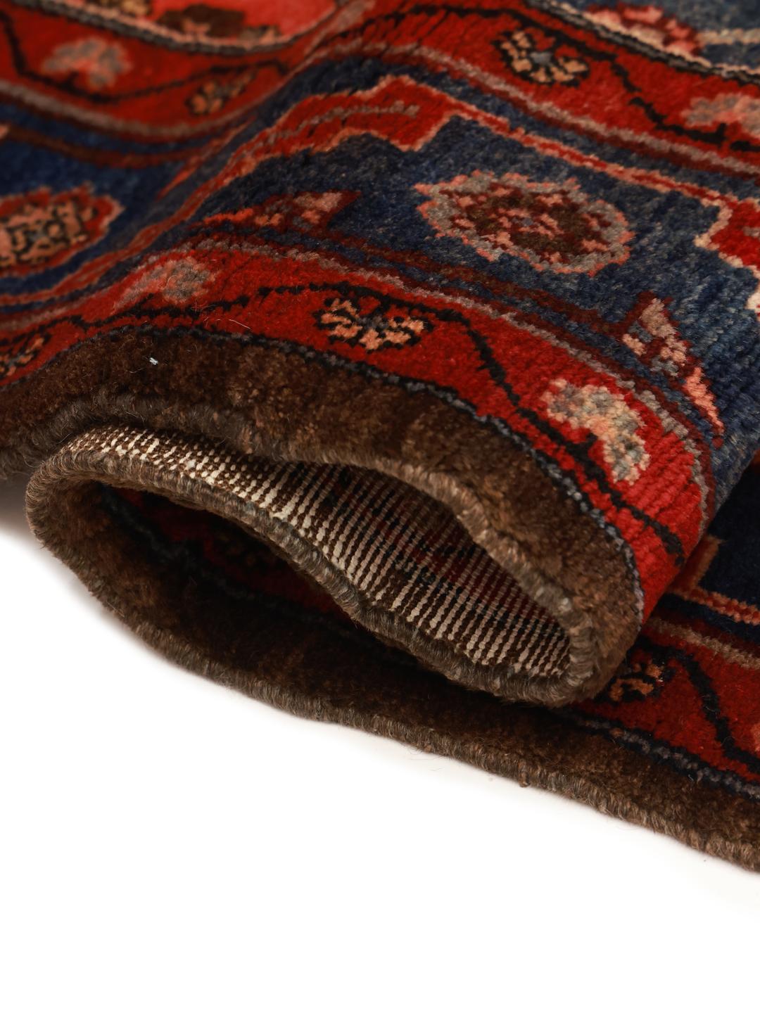 Een handgeknoopt Koliai tapijt met ingewikkelde geometrische motieven in diepblauw, rood en bruin.