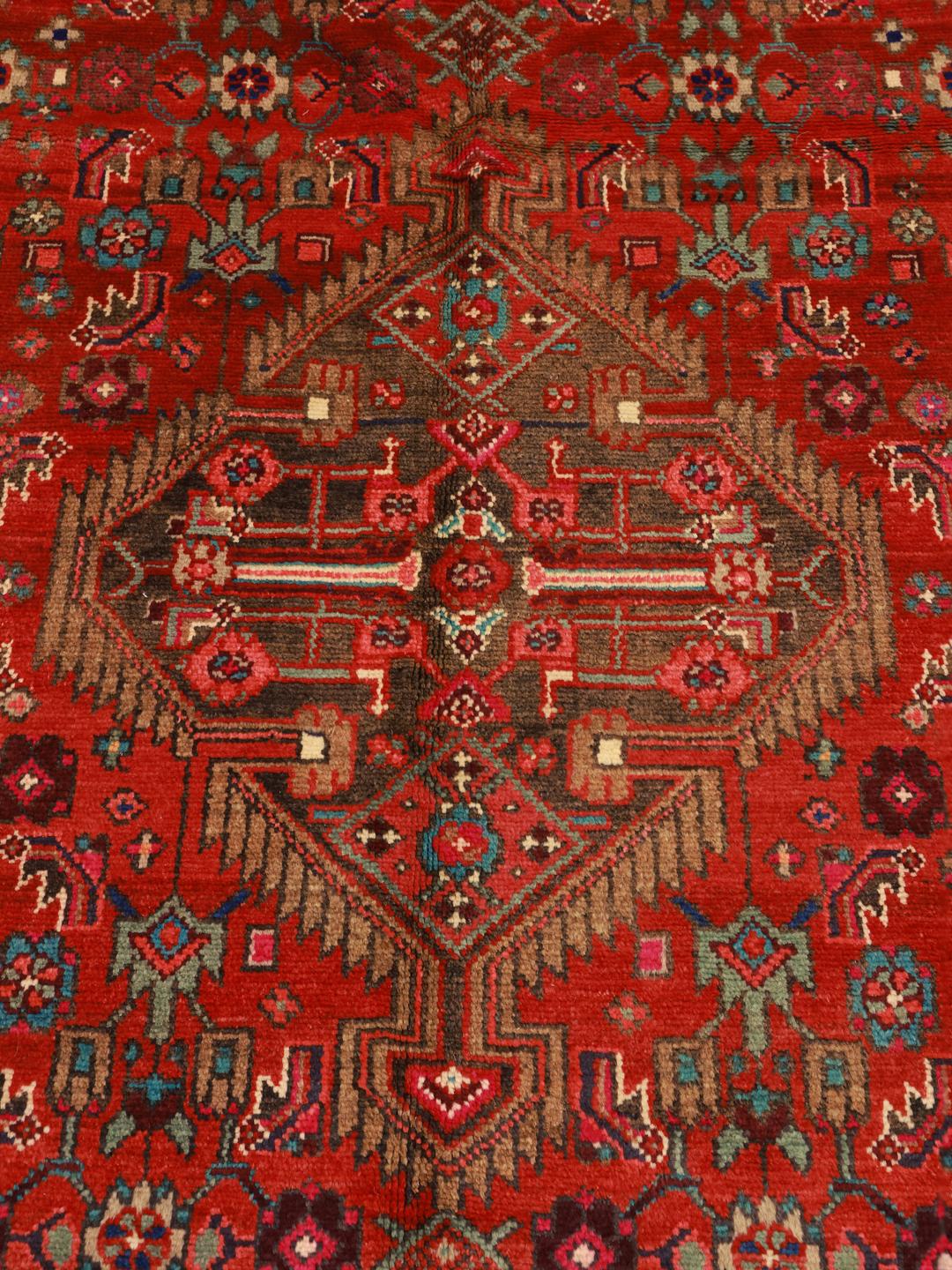 A vibrant hand-knotted rug from the Middle East with a deep red field and ornate tribal motifs.