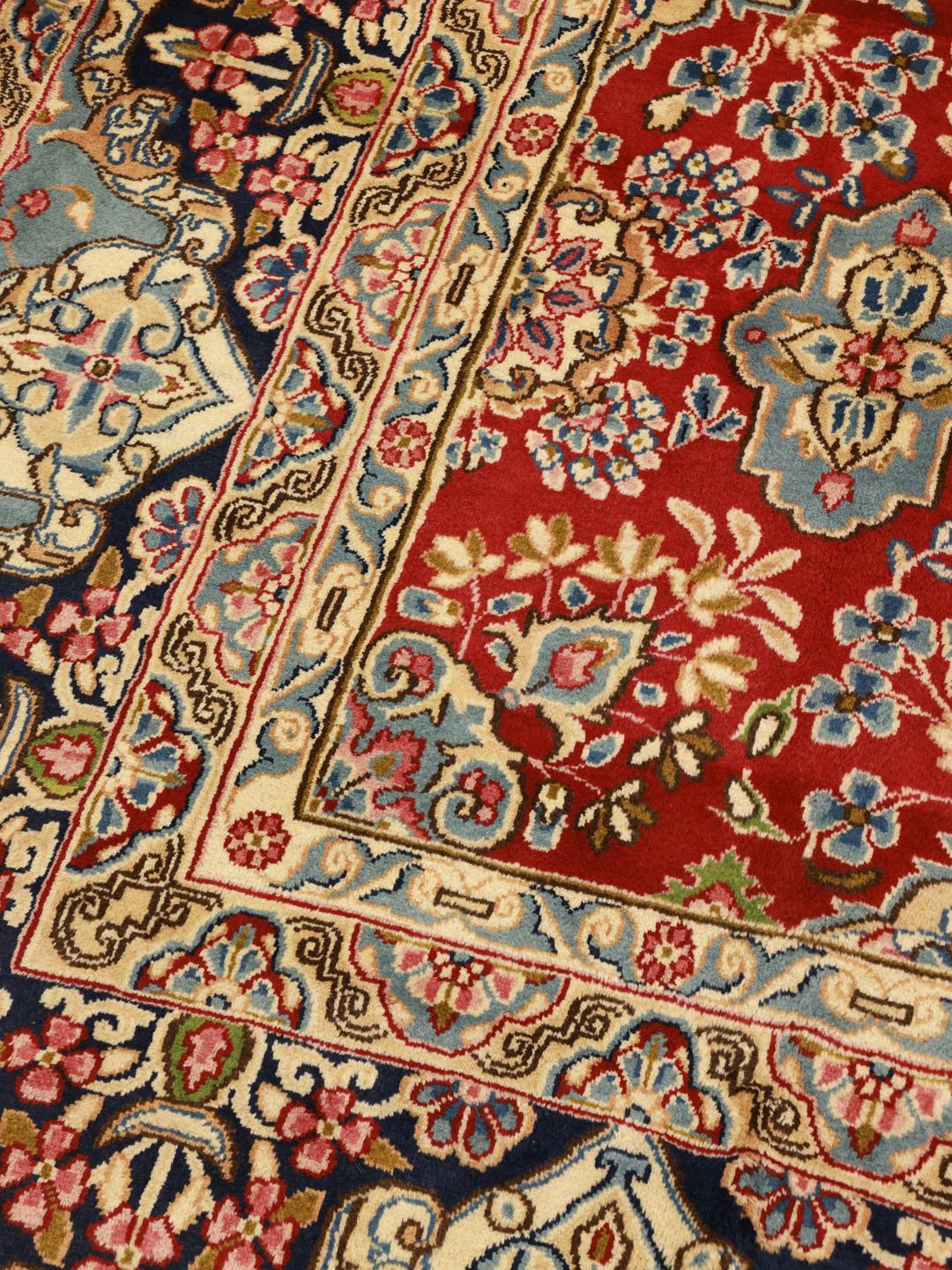 Een handgeknoopt Kerman tapijt uit het Midden-Oosten met een rood veld en verfijnde bloempatronen.