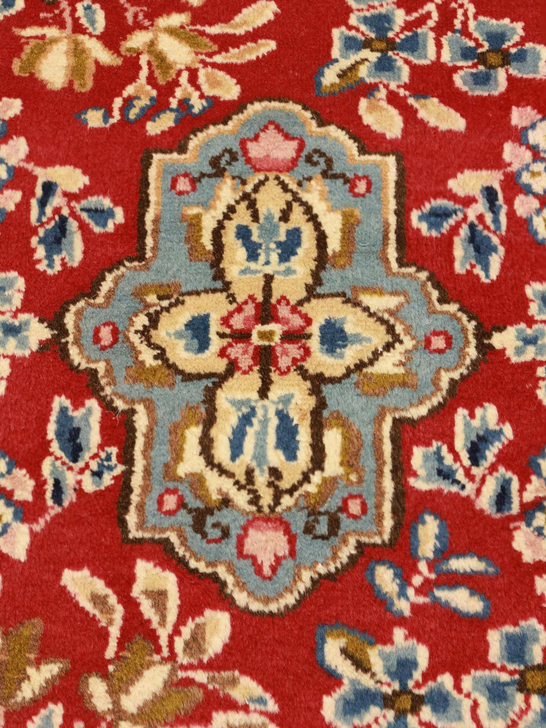 Een handgeknoopt Kerman tapijt uit het Midden-Oosten met een rood veld en verfijnde bloempatronen.