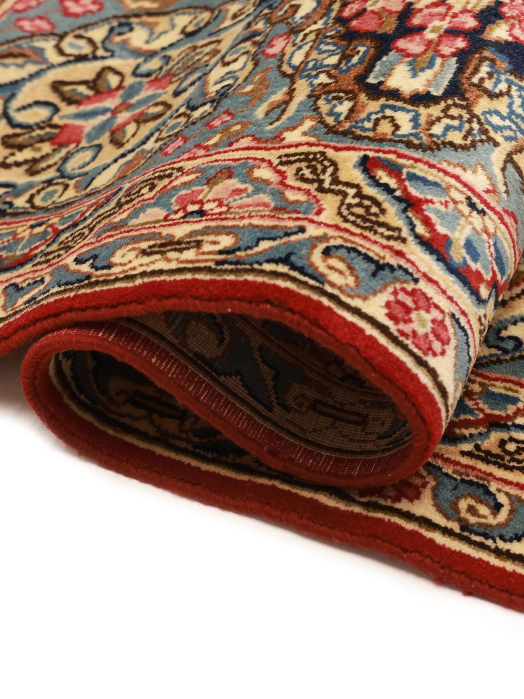 Een handgeknoopt Kerman tapijt uit het Midden-Oosten met een rood veld en verfijnde bloempatronen.