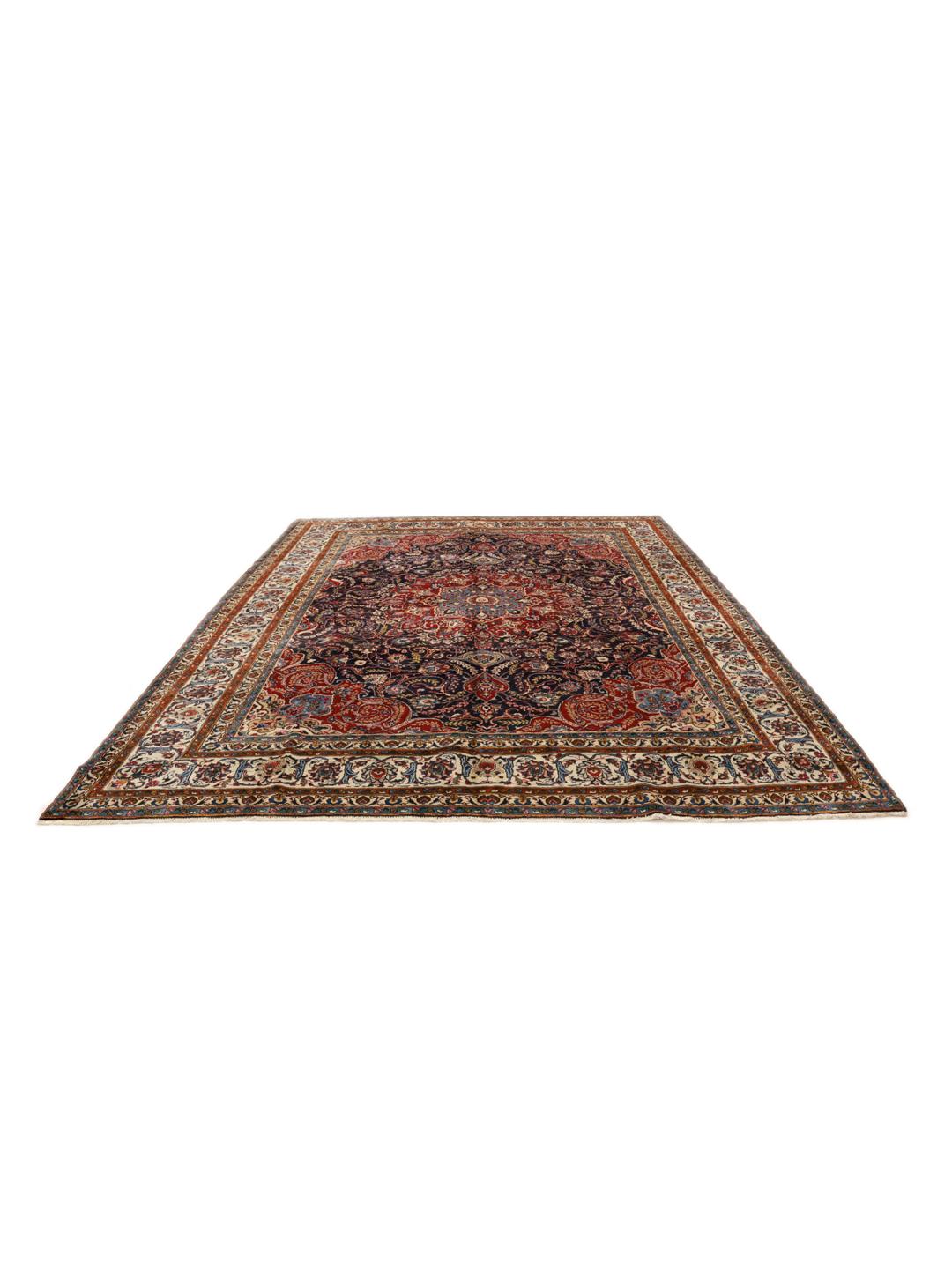 A large, hand-knotted Mashad rug from the Middle East with a dark-blue field and ornate floral medallion in shades of red and blue.