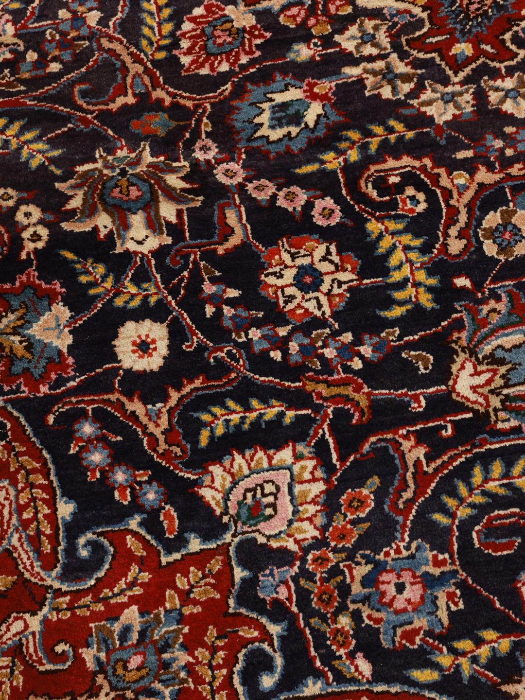 A large, hand-knotted Mashad rug from the Middle East with a dark-blue field and ornate floral medallion in shades of red and blue.