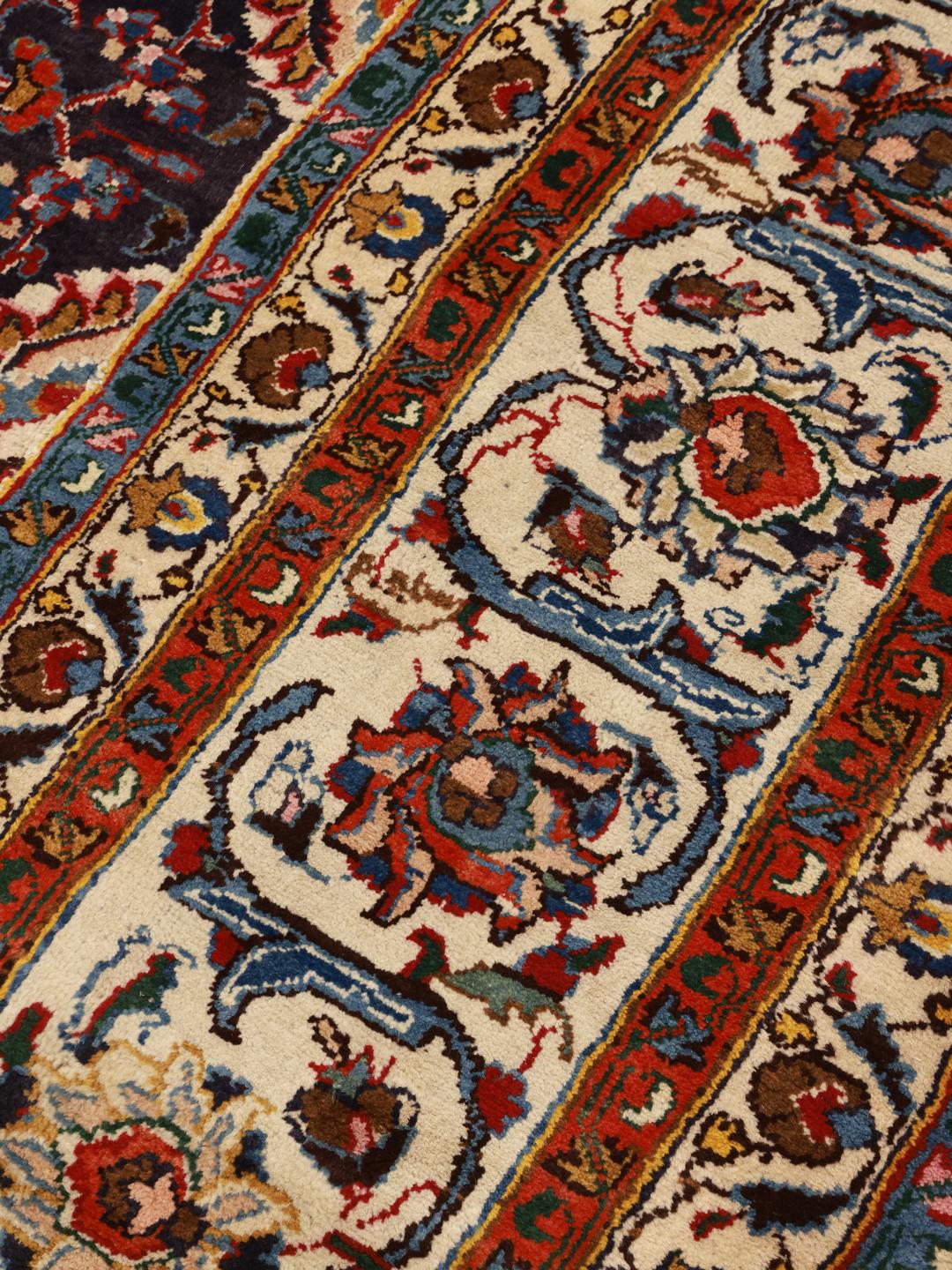 A large, hand-knotted Mashad rug from the Middle East with a dark-blue field and ornate floral medallion in shades of red and blue.