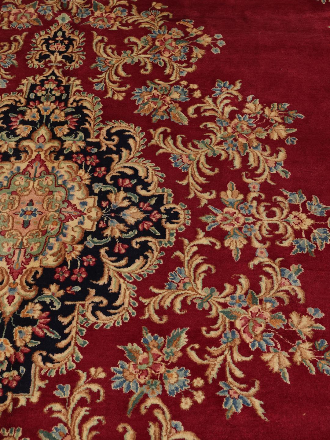 A hand-knotted Kerman rug from the Middle East with a dark-red field and floral patterns.
