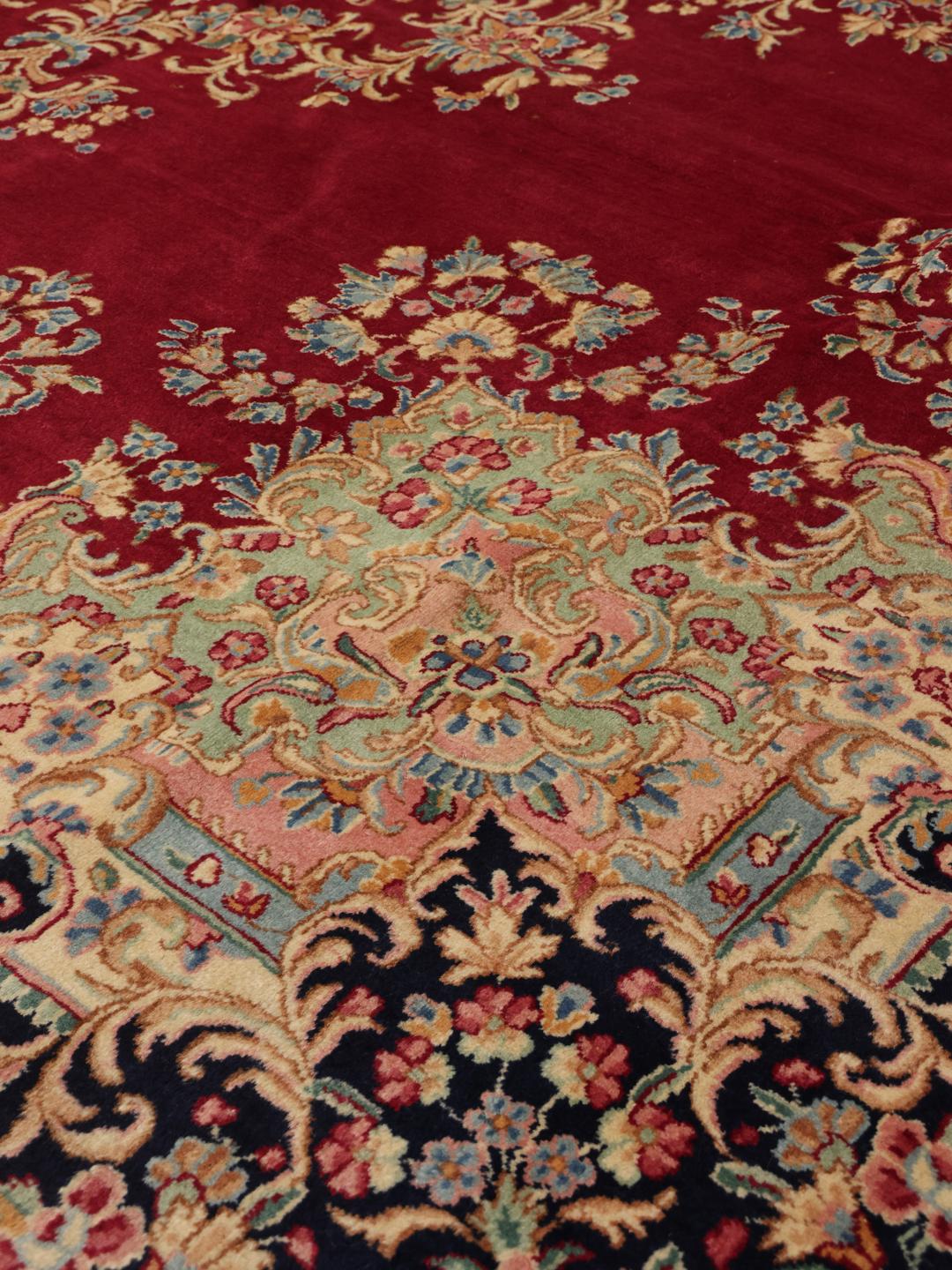 A hand-knotted Kerman rug from the Middle East with a dark-red field and floral patterns.