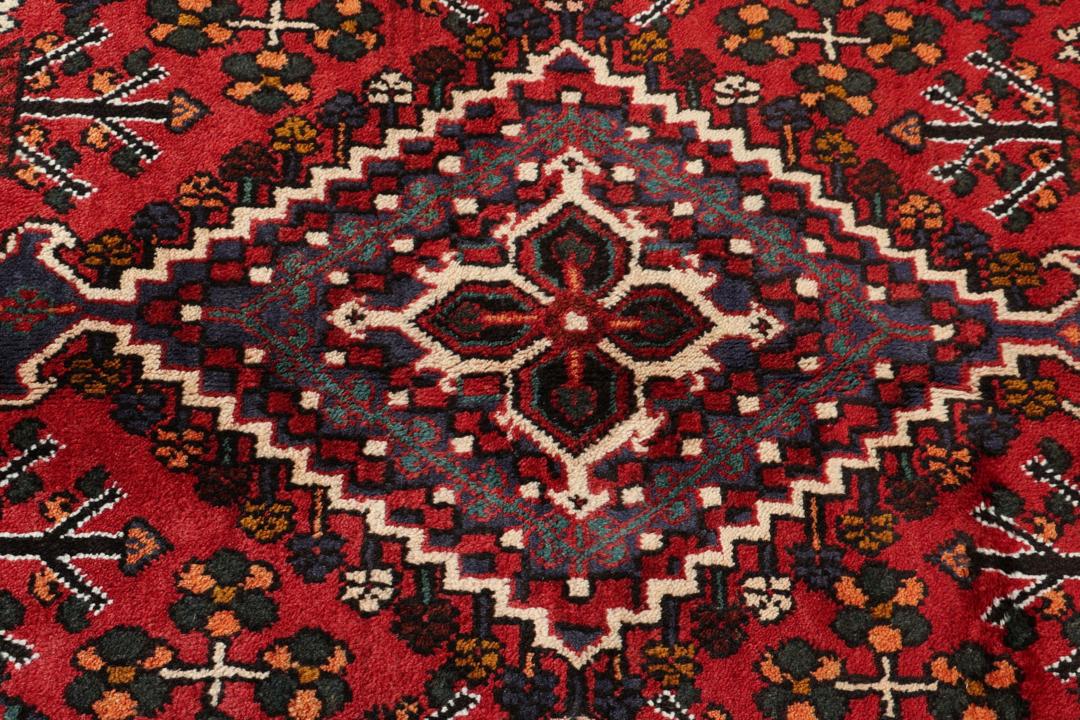Een handgeknoopt Joshaghan-tapijt uit het Midden-Oosten met een rood en blauw geometrisch medaillonpatroon.