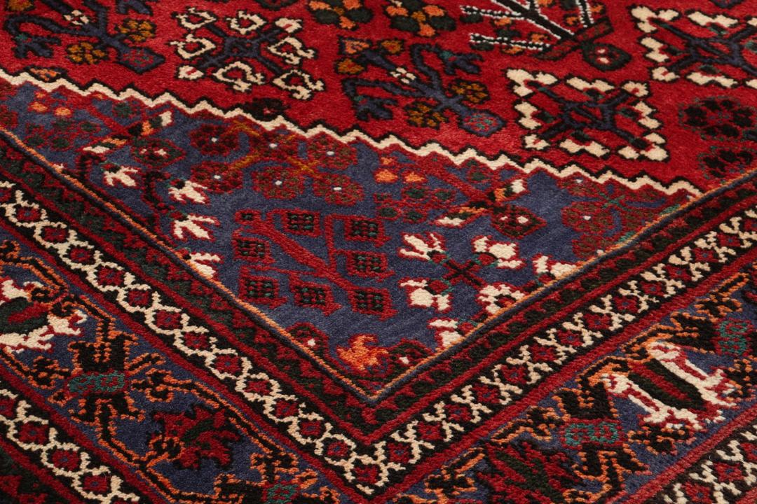 Een handgeknoopt Joshaghan-tapijt uit het Midden-Oosten met een rood en blauw geometrisch medaillonpatroon.