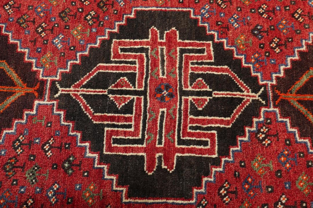 Een handgeknoopt Shiraz-tapijt uit het Midden-Oosten met een levendig rood en donkergrijs palet met geometrische tribale patronen.
