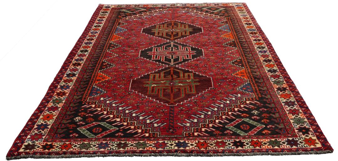 Een handgeknoopt Shiraz-tapijt uit het Midden-Oosten met een levendig rood en donkergrijs palet met geometrische tribale patronen.