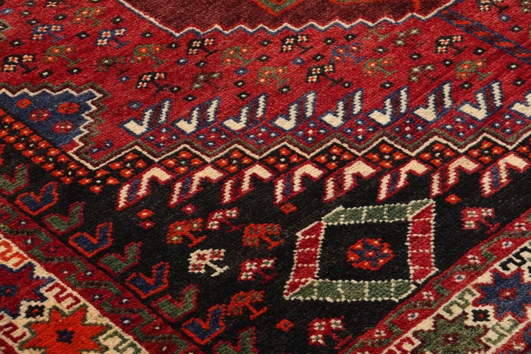 Een handgeknoopt Shiraz-tapijt uit het Midden-Oosten met een levendig rood en donkergrijs palet met geometrische tribale patronen.