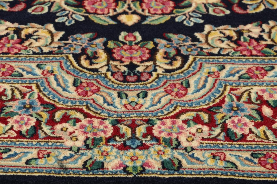 Et håndknyttet Kerman-tæppe fra Mellemøsten med et mørkeblåt felt og blomstermønstre.