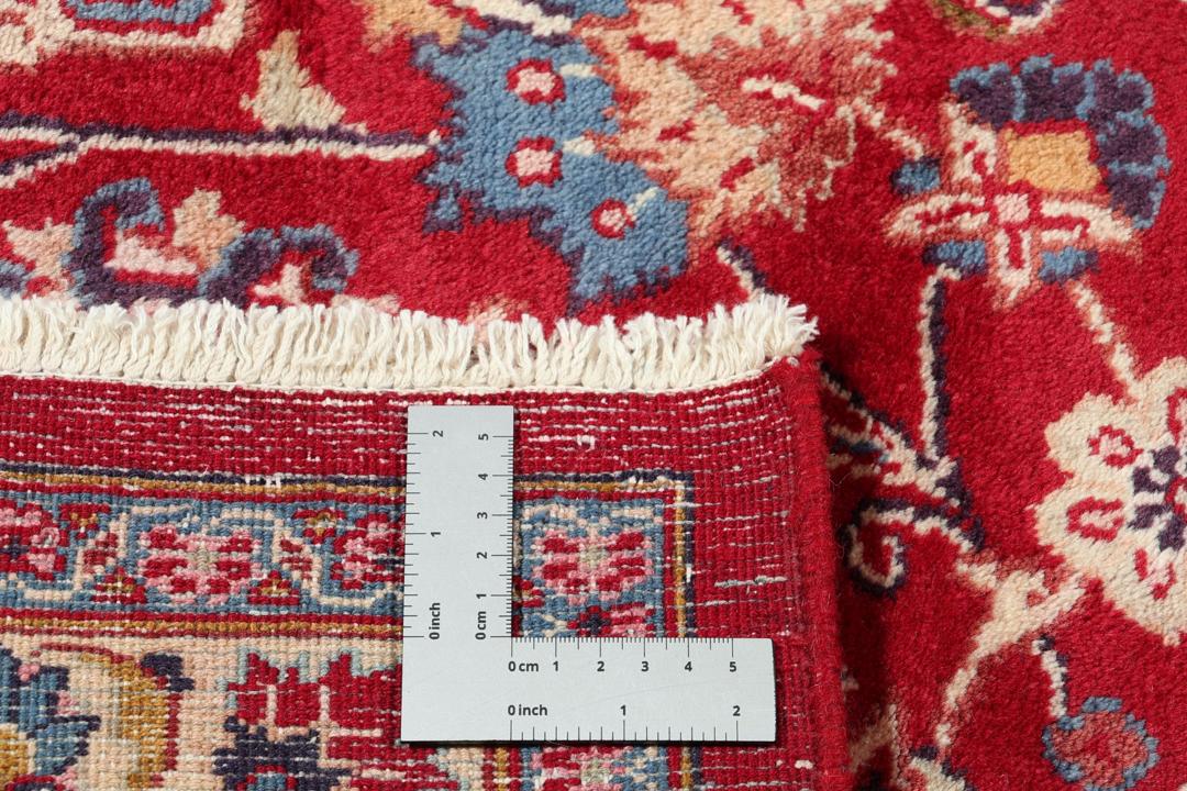 Een handgeknoopt Mashad-tapijt uit het Midden-Oosten met een rood veld en een gedetailleerd bloemmedaillon.