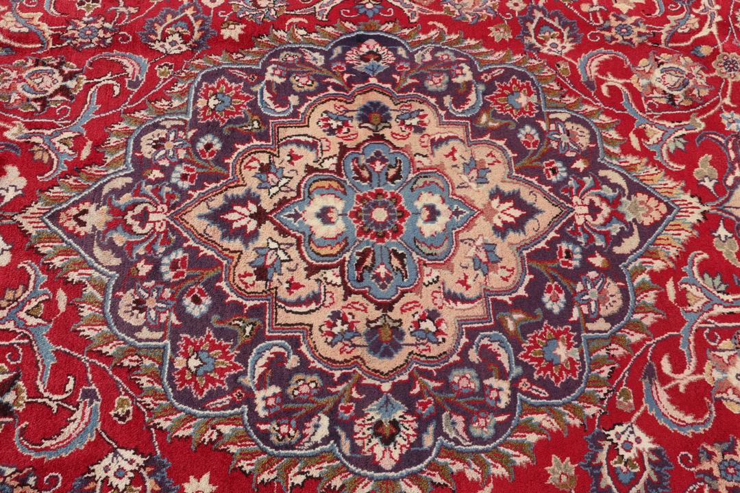 Een handgeknoopt Mashad-tapijt uit het Midden-Oosten met een rood veld en een gedetailleerd bloemmedaillon.