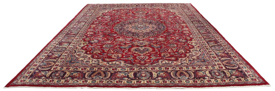 Een handgeknoopt Mashad-tapijt uit het Midden-Oosten met een rood veld en een gedetailleerd bloemmedaillon.