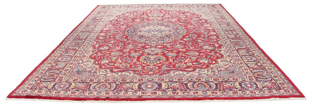 Een handgeknoopt Mashad-tapijt uit het Midden-Oosten met een rood veld en een gedetailleerd bloemmedaillon.