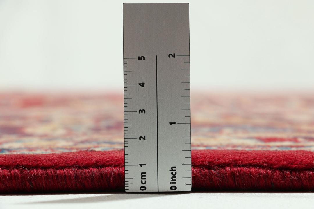 Een handgeknoopt Mashad-tapijt uit het Midden-Oosten met een rood veld en een gedetailleerd bloemmedaillon.