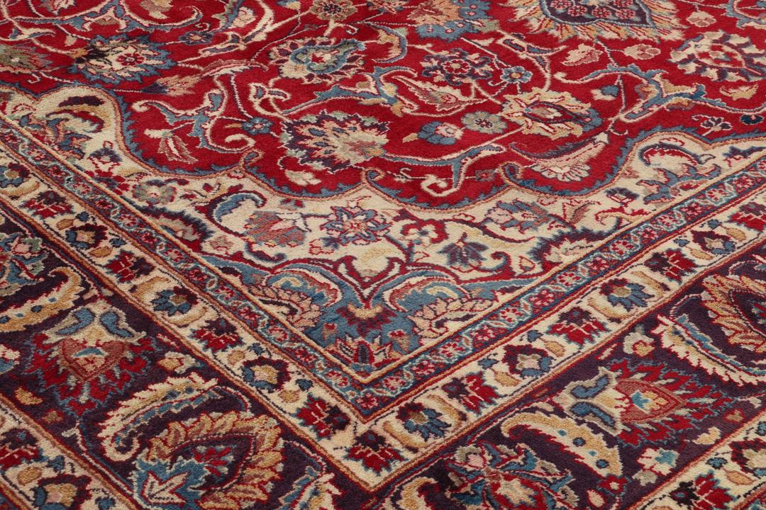 Een handgeknoopt Mashad-tapijt uit het Midden-Oosten met een rood veld en een gedetailleerd bloemmedaillon.