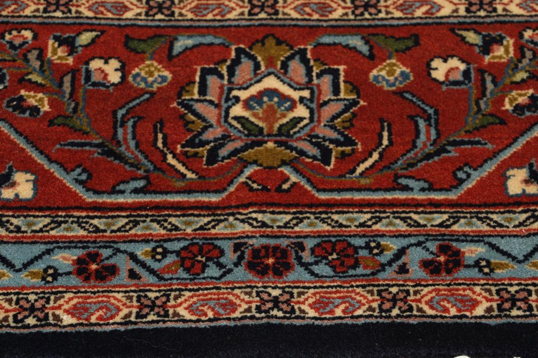A large rectangular hand-knotted Sarough rug from the Middle East with a dark-blue field and floral patterns.