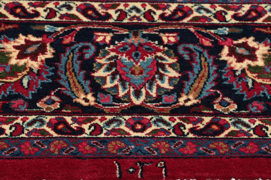 Een groot rechthoekig handgeknoopt Mashad-tapijt uit het Midden-Oosten met een rood veld en verfijnde bloemmotieven.