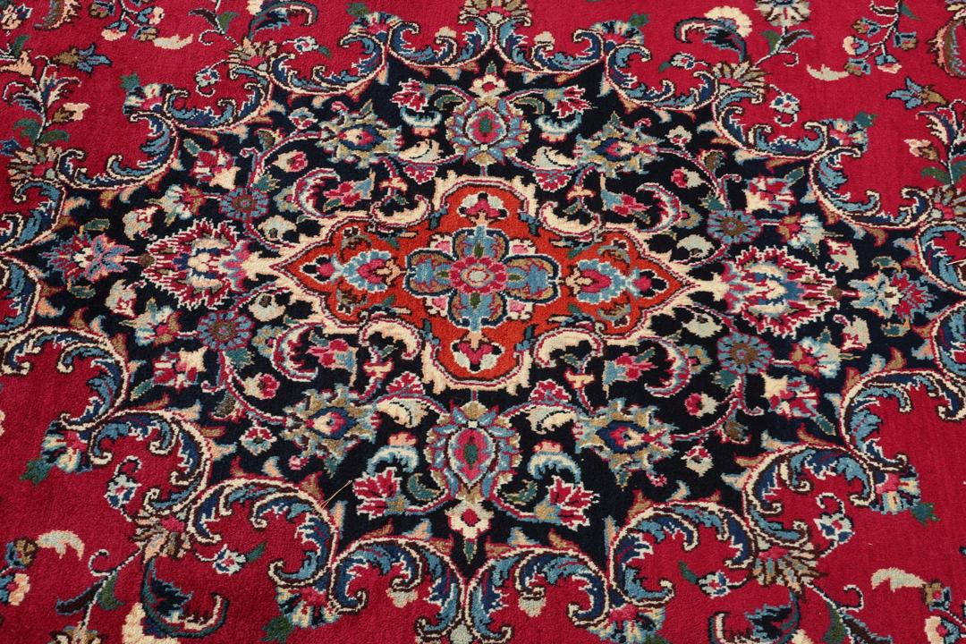 Een groot rechthoekig handgeknoopt Mashad-tapijt uit het Midden-Oosten met een rood veld en verfijnde bloemmotieven.
