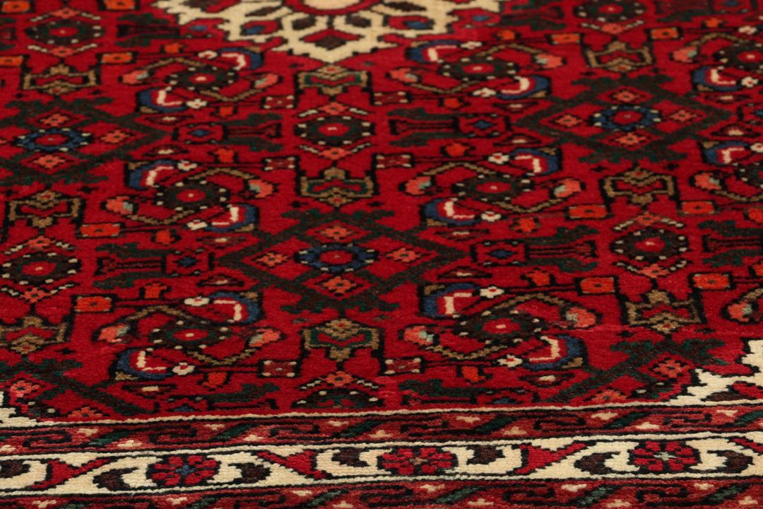 Een handgeknoopte Hosseinabad loper met een dieprood veld en geometrische medaillons.