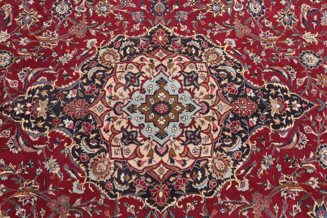 A hand-knotted Mashad rug from the Middle East with a deep red field and intricate floral medallion.