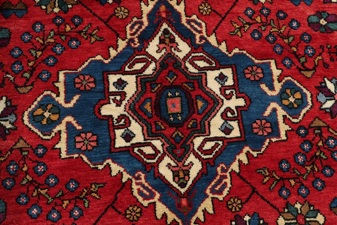 Een handgeknoopt Hamadan-tapijt uit het Midden-Oosten met een rood en blauw medaillonontwerp.