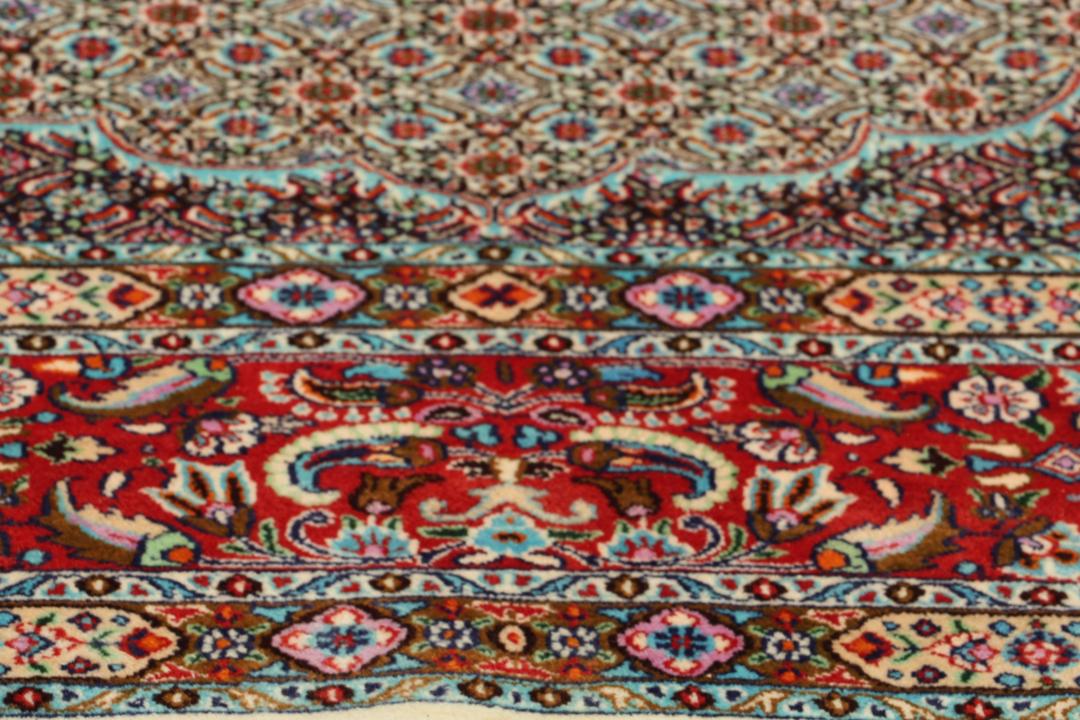 A large rectangular Moud rug from the Middle East featuring a central medallion and ornate floral patterns in multicolor wool.