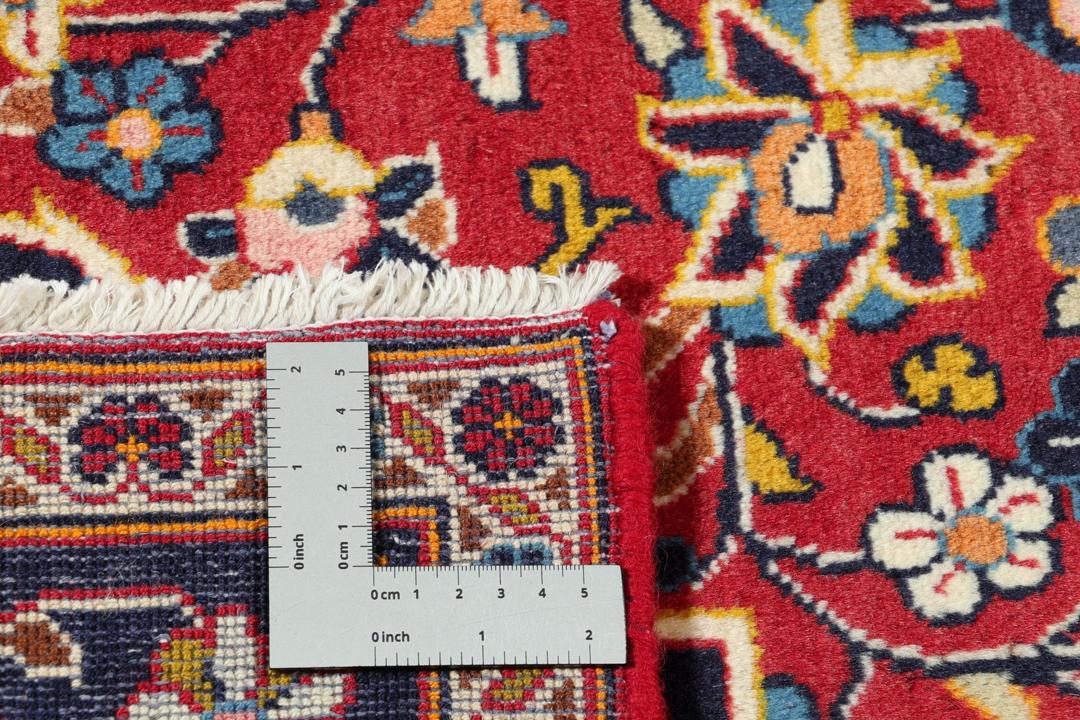Een handgeknoopt Kashan-tapijt uit het Midden-Oosten met een rood veld en een blauw medaillon.