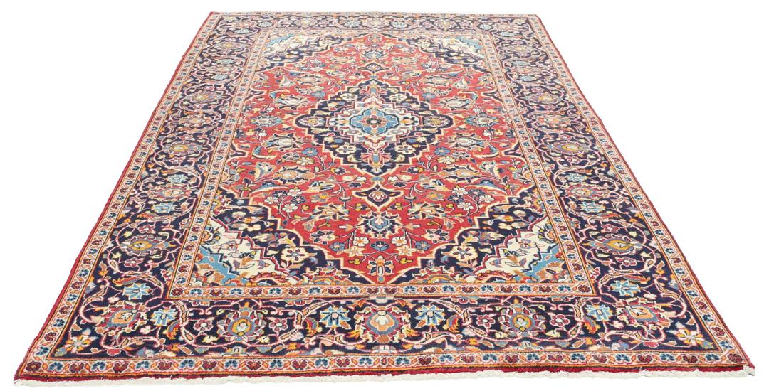 Een handgeknoopt Kashan-tapijt uit het Midden-Oosten met een rood veld en een blauw medaillon.
