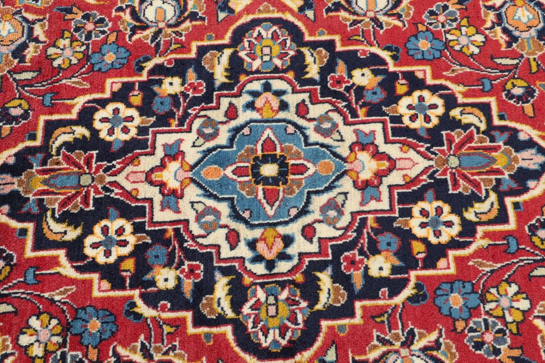 Een handgeknoopt Kashan-tapijt uit het Midden-Oosten met een rood veld en een blauw medaillon.