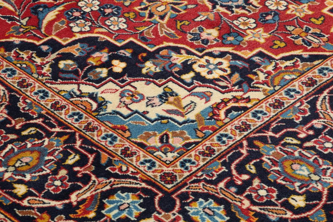 Een handgeknoopt Kashan-tapijt uit het Midden-Oosten met een rood veld en een blauw medaillon.