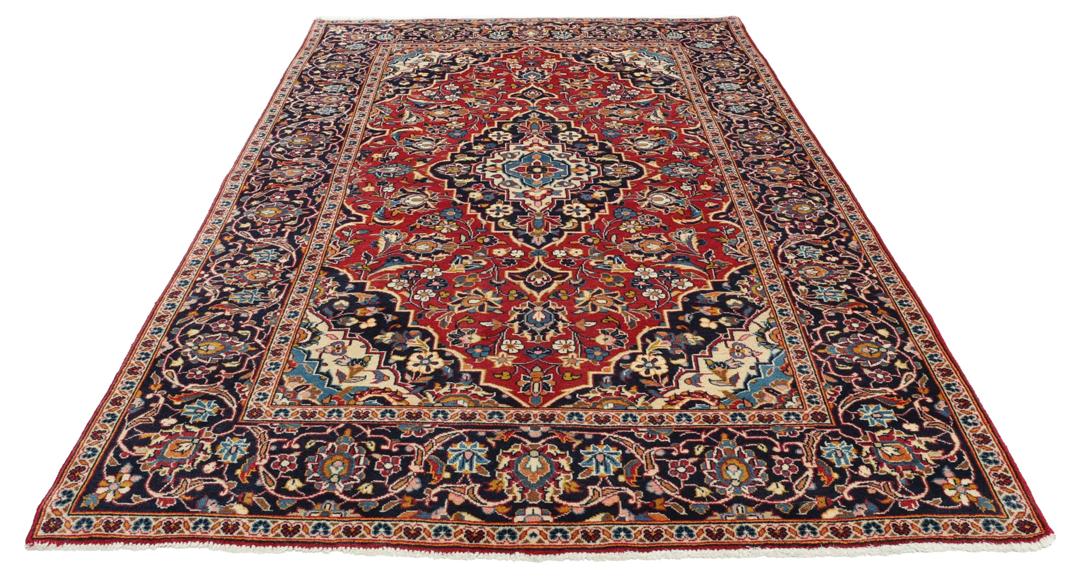 Een handgeknoopt Kashan-tapijt uit het Midden-Oosten met een rood veld en een blauw medaillon.