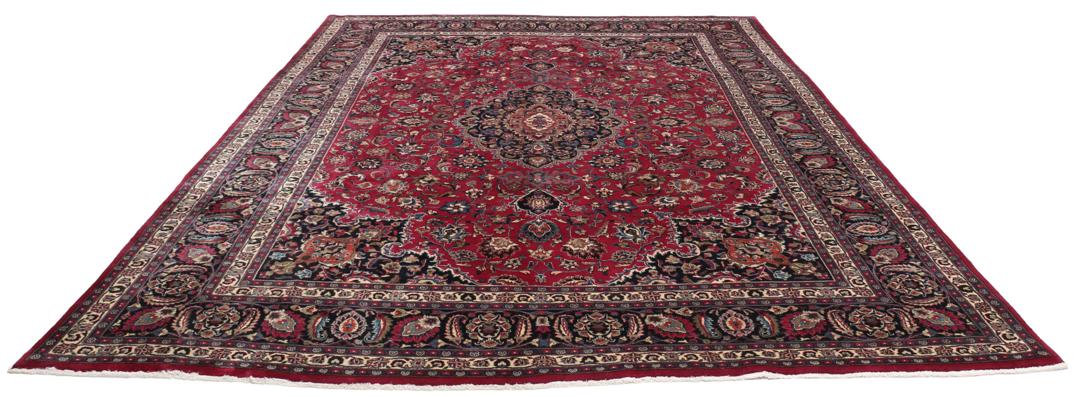 A large, hand-knotted Mashad rug from the Middle East with a deep red field and floral motifs.