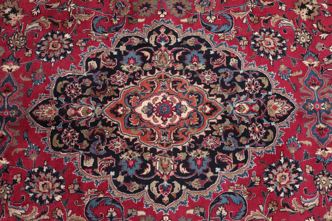 A large, hand-knotted Mashad rug from the Middle East with a deep red field and floral motifs.