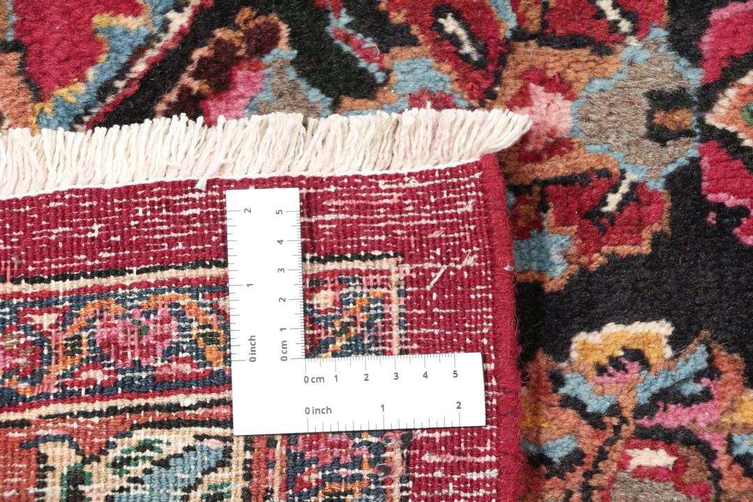 A large, hand-knotted Mashad rug from the Middle East with a deep red field and floral motifs.