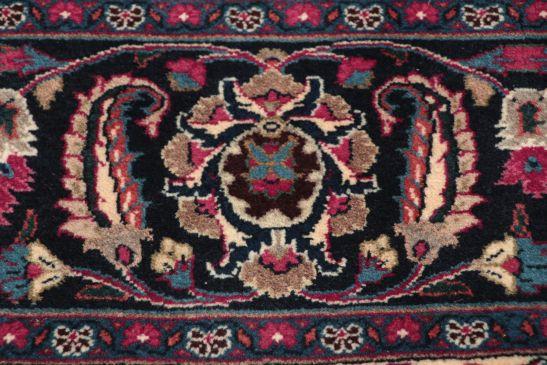 A large, hand-knotted Mashad rug from the Middle East with a deep red field and floral motifs.