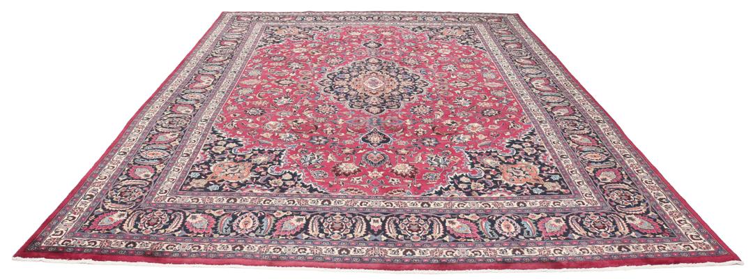 A large, hand-knotted Mashad rug from the Middle East with a deep red field and floral motifs.