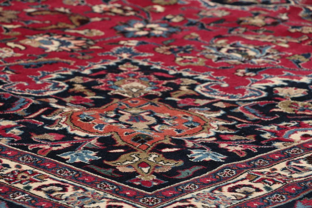 A large, hand-knotted Mashad rug from the Middle East with a deep red field and floral motifs.