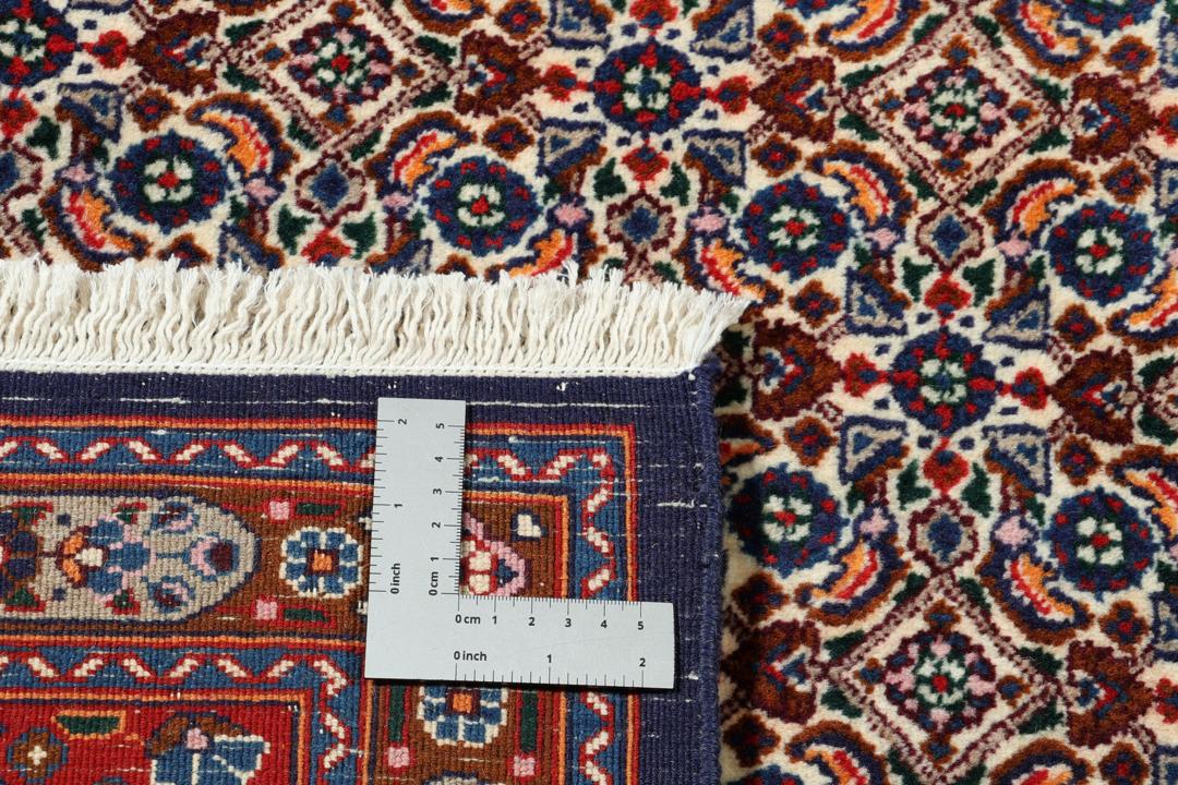 Een handgeknoopt Moud-tapijt uit het Midden-Oosten met een rood en blauw medaillonpatroon.