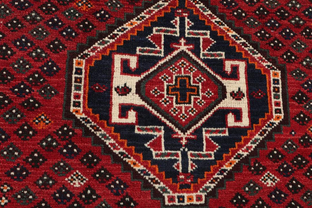 Een handgeknoopt rood Shiraz-tapijt met geometrische patronen en een decoratieve rand.