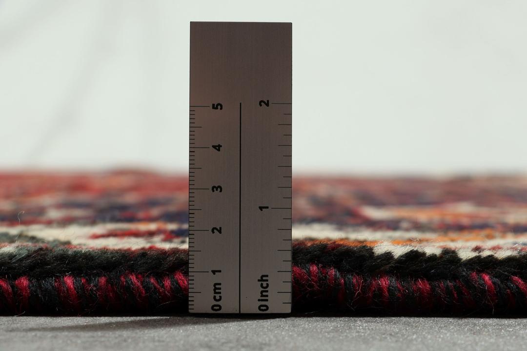 Een handgeknoopt rood Shiraz-tapijt met geometrische patronen en een decoratieve rand.