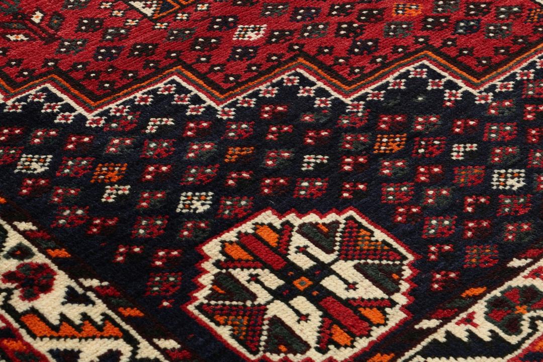 Een handgeknoopt rood Shiraz-tapijt met geometrische patronen en een decoratieve rand.