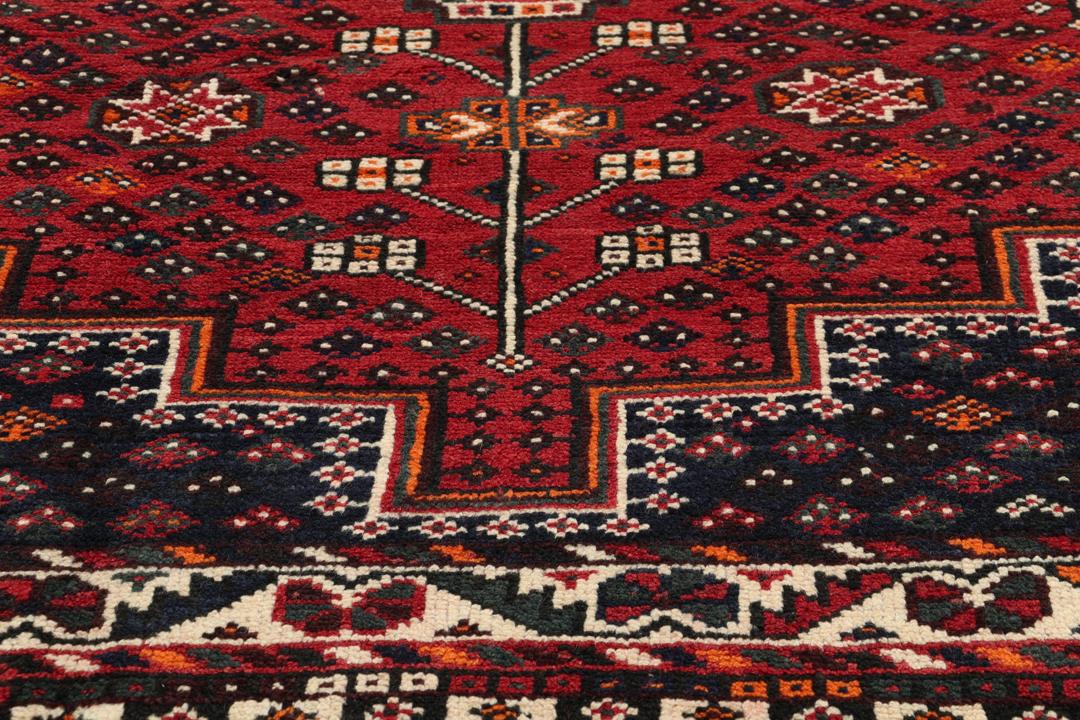 Een handgeknoopt rood Shiraz-tapijt met geometrische patronen en een decoratieve rand.